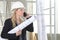 Woman architect or construction engineer talk on the mobile phone wear helmet and holds blueprint inside a building site with