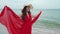 Woman with arms spread in a red dress on the sea beach with wind blow