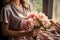 Woman arranging vibrant peony bouquet on rustic craft paper table in natural light-filled room