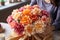 Woman arranging vibrant peony bouquet on rustic craft paper table in natural light-filled room