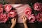 Woman arranging vibrant peony bouquet on rustic craft paper table in natural light-filled room