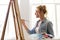 Woman artist with easel painting at art studio