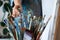 Woman artist hand choosing and picking oil paintbrushes near canvas in workshop