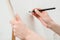 Woman artist`s hand with a large simple pencil, draws on a clean white canvas, close-up.