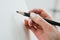 Woman artist`s hand with a large simple pencil, draws on a clean white canvas, close-up.