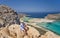 Woman artist sits on the stones and paints a picture of Tigani cape and Balos lagoon with sandy beach. Crete, Greece