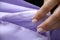 A woman attaches a cambric cloth to satin fabric. Seamstress collects lilac fabric closeup.