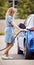 Woman Attaching Charging Cable To Environmentally Friendly Zero Emission Electric Car Outdoors