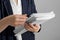 Woman attaching documents with metal binder clip on grey background, closeup