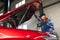 Woman auto mechanic opens the hood of a car in a car service.