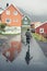 Woman with backpack running on wet street after rain. cozy Scandinavian houses reflecting on the street.