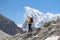 Woman with backpack walks in Himalayas on the slope of glacier with mountain peak in the background