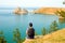 A woman backpacker looks at the Shamanka Rock, Cape Burhan on Olkhon Island. Lake Baikal, Russia