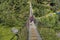 Woman backpacker on trekking path crossing a suspended bridge