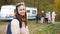 A woman with badminton rackets stands against the background of a travel trailer and a rejoicing family in an autumn