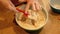 Woman baker hand mixes cookie dough ingredients in a green bowl.