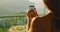 A woman on a balcony uses her phone to photograph the scenic view of the Amalfi Coast, with a breakfast table nearby.
