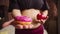 Woman with a bare fat belly holds a donut and an apple, close-up. Fat woman chooses doughnut. Concept of diet and
