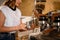 woman barista holds steel jug and makes whipped cream using coffee machine.