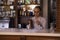 Woman bartender rubs the glass in cafe. Girl barista in casual clothes smiling and using rag wiping glass at counter in