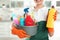 Woman with basin of detergents and bottle in kitchen. Cleaning service