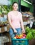 woman with basket with fresh greengrocery enjoying purchases in vegetable store