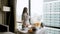 Woman in bathrobe eating breakfast near window with city view