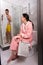 Woman in bathrobe with newspaper sitting on a toilet and waiting