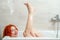 Woman in bathroom lying, raised legs up, laughing, looking at camera. Purity, relaxation, joy