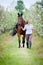 Woman and bay horse in apple garden. Horse and beautiful lady walking outdoor.