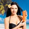 Woman on the beach holds orange sun tan lotion bottle.