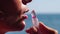 Woman, beach, lipstick - pretty lady applies protective lipstick for lip care. On beach, woman uses nourishing lipstick