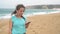 Woman on beach listening to music on headphones from smart phone. Nazare, Portugal