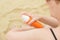 Woman on the beach puts sunscreen cream on hands from an orange bottle