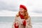 Woman beach in red beret scarf and mitts holding a cup of tea in his hands. Depicting beach relaxation and cozy attire