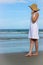 Woman On Beach Touching Hat And Looking At Ocean