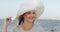 Woman, beach and wind with hat, smile and style with face in summer, vacation and outdoor by waves. Girl, sunhat and