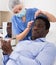 Woman beautician in mask examining face skin of afro american male patient