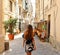 Woman in beautiful flowered dress walking in street of Syracuse, Sicily. Rear view of cheerful and happy girl in typical Italian