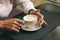 Woman with beautiful hands is drinking coffee in cafe. Close-up cappuccino in white cup, image with author processing.