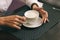 Woman with beautiful hands is drinking coffee in cafe. Close-up cappuccino in white cup, image with author processing.