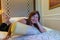 WOMAN ON BED LYING ON PILLOWS HOTEL ROOM SMILING POSING SOFT LIGHT