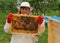 Woman Beekeeper holding frame of honeycomb with bees