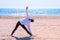 Woman beginner does triangle yoga pose sand sea beach sport exercise back view.