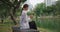 Woman on bench phone in hand near water lake city public park side view skyscrapers behind. City park serene nature