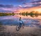 Woman with bicycle on the coast of the river at sunset in summer