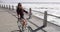 Woman, bicycle and freedom on promenade, smile and vacation at beach, sea and waves by ocean. Female person, tourism and