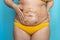 Woman with big stomach and buttocks in yellow underwear smear coffee body scrub on belly closeup. Doing tummy massage