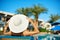 Woman in big white hat lying on a lounger near the swimming pool at the hotel, concept summer time to travel