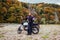 Woman biker travel by motorbike in fall. Motorcyclist enjoys autumn landscape in mountains having rest by forest